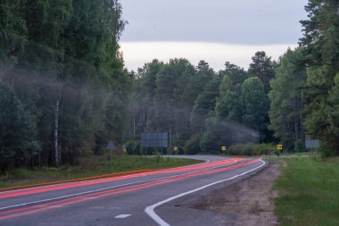 Ormanda uzun bir kepenk açma hızıyla yoldan geçen bir araba. Potansiyel tehlikeli sürüş koşulları
