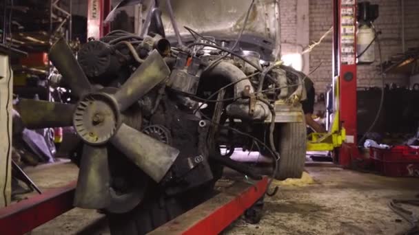 Taller de reparación de coches, o desmontaje del coche. En el ascensor cuelga el motor sacado del coche. — Vídeos de Stock