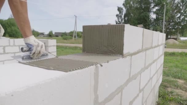 Metselaar leggen muur van een blok, met een spatel voor stopverf in de open lucht. — Stockvideo