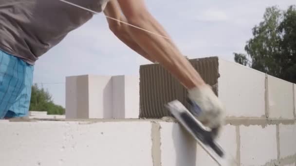 Batu bata meletakkan dinding dari blok, dengan spatula untuk dempul di udara terbuka. — Stok Video