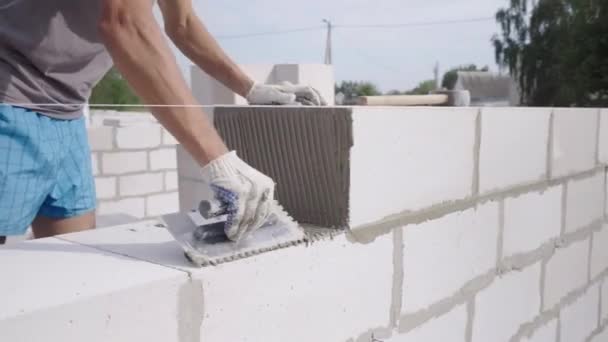 Metselaar leggen muur van een blok, met een spatel voor stopverf in de open lucht. — Stockvideo