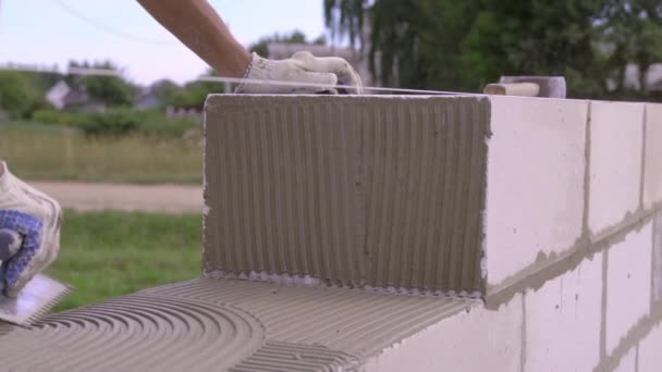 Batu bata meletakkan dinding dari blok, dengan spatula untuk dempul di udara terbuka. — Stok Video