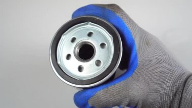 Ustanın eli, kamera üzerinde beyaz arkaplanda araba yağı filtresi döndürür.