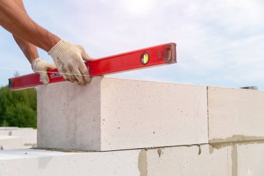 İnşaatçı blokların eğilim seviyesini kontrol eder. İnşaatçı, bir konut binasının inşaat sahasına beton bloklardan yapılmış bir duvar inşa ediyor. Bir ev inşa etmenin dışında