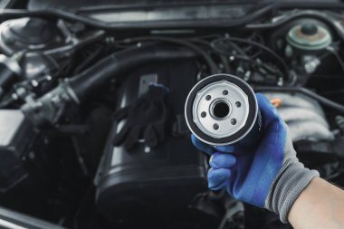Yağ filtresini değiştiriyorum. Araba motor tamircisi elinde bir yağ filtresi tutuyor açık bir arabanın arka planına karşı.