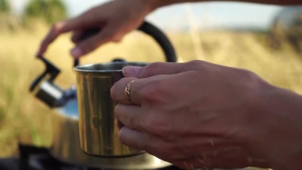 Las manos de las mujeres, vierten el agua en una taza de hierro de una tetera. en la naturaleza, — Vídeos de Stock