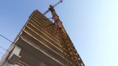 İnşaat halindeki bir gökdelenin altından bir manzara ve gökyüzüne karşı bir vinç..