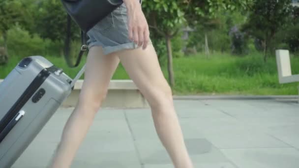 Los pies de las mujeres caminan en la acera y llevan una maleta detrás de ellos. — Vídeos de Stock