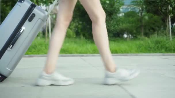Ženské nohy kráčejí po chodníku a nesou za sebou kufr. — Stock video