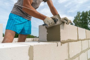 İnşaatçı beton karışımını yapı bloğuna uygulamak için çentik mala kullanır. Ev inşa etme kavramı