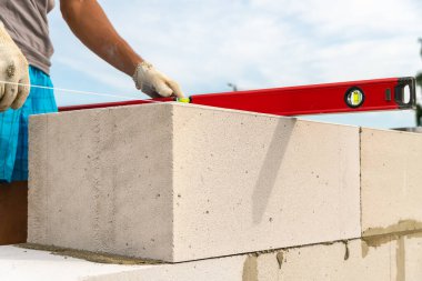 İnşaatçı blokların eğilim seviyesini kontrol eder. İnşaatçı, bir konut binasının inşaat sahasına beton bloklardan yapılmış bir duvar inşa ediyor. Bir ev inşa etmenin dışında