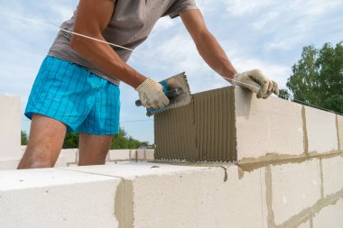 İnşaatçı beton karışımını yapı bloğuna uygulamak için çentik mala kullanır. Ev inşa etme kavramı