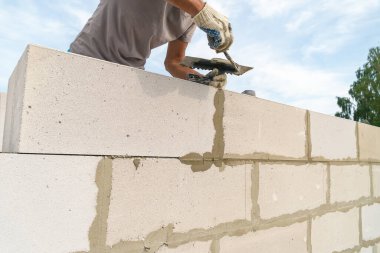İşçi dikişleri bir spatulayla siliyor. Tuğlacı işçi açık havada müstakbel bir evin beyaz bloklarını diziyor..