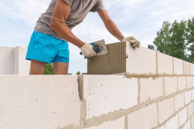İnşaatçı çimento karışımını havalandırılmış beton bloklara uygulamak için çentikli bir mala kullanıyor. Özel bir ev inşa etme fikri