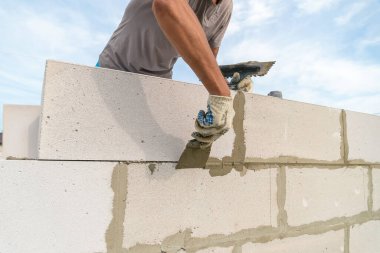 İşçi dikişleri bir spatulayla siliyor. Tuğlacı işçi açık havada müstakbel bir evin beyaz bloklarını diziyor..