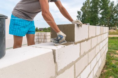 İnşaatçı çimento karışımını havalandırılmış beton bloklara uygulamak için çentikli bir mala kullanıyor. Özel bir ev inşa etme fikri