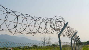Gün batımında havaalanının etrafını saran dikenli teller, dağların arka planına karşı.
