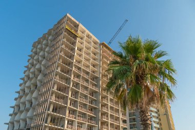 Güneşli bir yaz gününde, çok katlı bir evin inşaatı mavi gökyüzünün arka planına, Georgia, Batumi 'de palmiye ağaçlarına karşıdır.