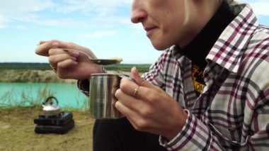 Beyaz saçlı bir kadın, yakın plan, kaşıkla metal bir bardaktan yemek yiyor..