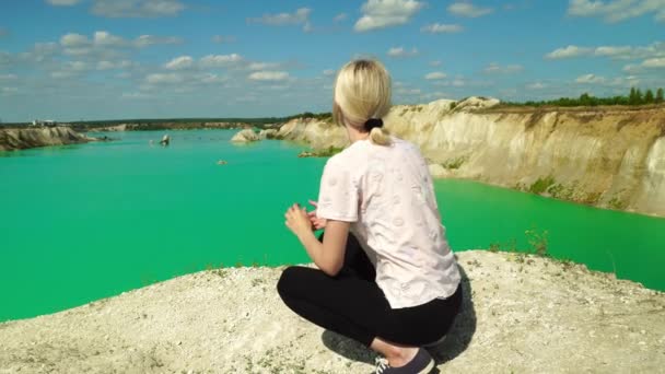 En kvinnlig turist sitter på stranden av en damm med turkost vatten. — Stockvideo