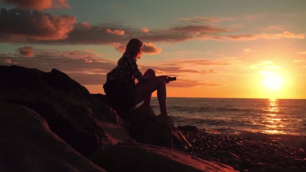 Silueta de mujer esbelta en la playa al atardecer hermoso, ella sentada soñando — Vídeos de Stock