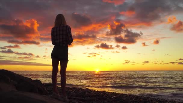 Silhouet van slanke vrouw op het strand bij mooie zonsondergang, ze staat en droomt — Stockvideo