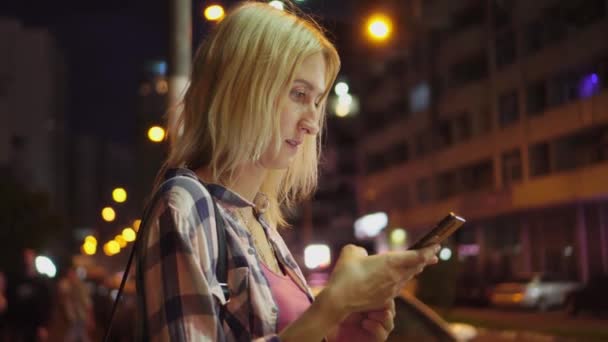 네온 불빛 이 가득 한 야간 도시 거리인 스마트폰을 사용하는 여성의 손에 집중하라. — 비디오