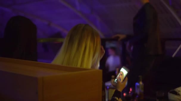 Una joven en un club nocturno toma una selfie en su teléfono, sentado en una mesa. — Vídeo de stock