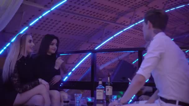 Jongens en meisjes ontspannen aan een tafel in een nachtclub. Ze lachen, drinken, praten. . — Stockvideo