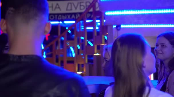 Молодой парень в кожаной куртке, молодые девушки стоят возле бара в клубе, разговаривают, веселятся, пьют алкоголь — стоковое видео