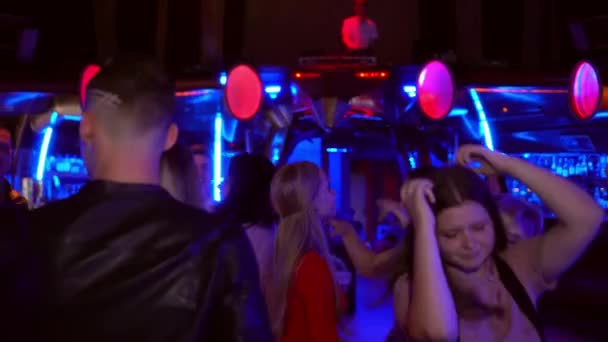 Tânărul într-o jachetă de piele intră în mulțime într-un club și dansează, o fată tânără într-o rochie roșie trece pe lângă el și se întoarce la ea. — Videoclip de stoc