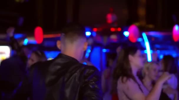 Jeune homme en veste de cuir entre dans la foule dans un club et danse, une jeune fille en robe rouge passe devant lui et il se retourne vers elle — Video