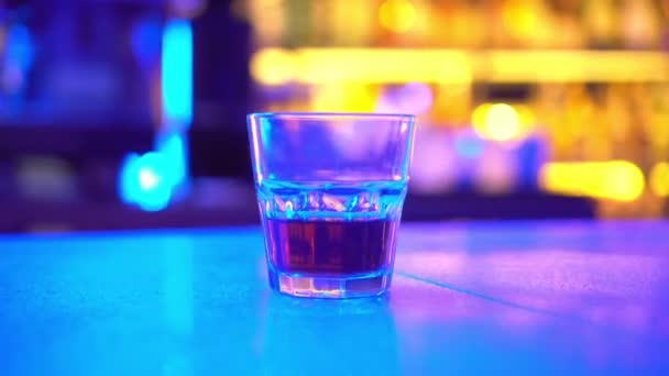 Ночной клуб, на баре есть стакан, наполненный алкоголем из бара, в неоновом свете. — стоковое видео