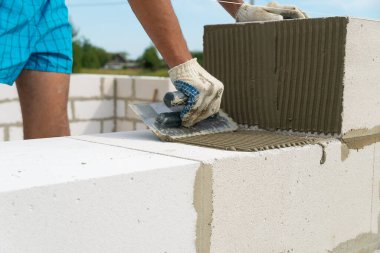 İnşaatçı inşaat bloğunun kenarlarına çimento karışımını uygulamak için çentik mala kullanır. Ev inşa etme kavramı
