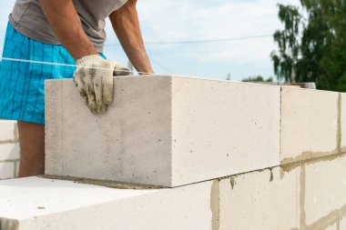 İnşaatçı, bir evin inşaat sahasında beton bloklardan bir duvar yapıyor. Bir ev inşa etme kavramı