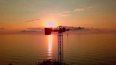 Gün batımında kuş bakışı bir vinç, güneş ışınları vinç yapısından geçer.