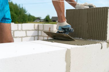 İnşaatçı inşaat bloğunun kenarlarına çimento karışımını uygulamak için çentik mala kullanır. Ev inşa etme kavramı