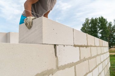 İnşaatçı, inşaat alanındaki beton bloklardan yapılmış beton duvarı kendi elleriyle inşa ediyor. Bir ev inşa etme kavramı