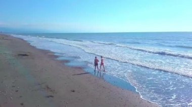 Bir adam ve bir kadın ıssız bir sahilde yürüyorlar, sörf yaparken..