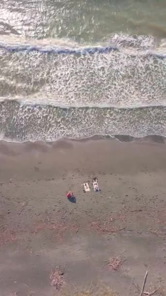 Drona, kobieta i dwóch mężczyzn opalają się i relaksują na pustej plaży nad morzem. — Wideo stockowe