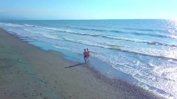 Un hombre y una mujer están caminando por una playa desierta, en el oleaje. — Vídeo de stock