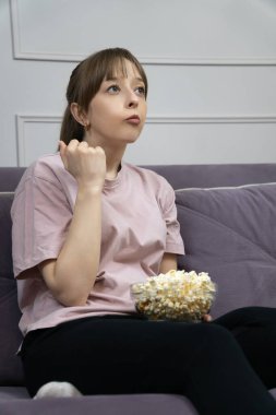 Sinema gecesinden zevk alan rahat bir kadın oturma odasında kanepede oturup ev eğlencesi yaşarken cam kaseden patlamış mısır yiyor. Dikey fotoğraf