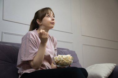 Genç kadın rahat bir koltukta oturmuş, büyüleyici bir film izlerken patlamış mısırın tadını çıkarıyor. Yüzündeki ifade, planla olan nişanını yansıtıyor.