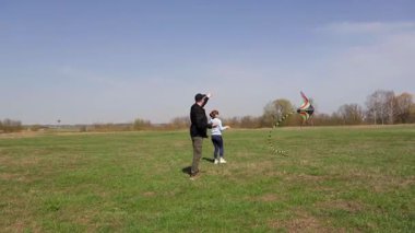 Mutlu genç bir çift açık güneşli bir günde yeşil bir alanda birlikte renkli bir uçurtma fırlatıyor açık hava aktivitelerinin tadını çıkarıyor ve onu uçurma başarılarından dolayı sevinçle gülümsüyor.