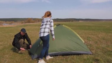Mutlu Kafkasyalı çift yeşil bir kubbeyi çimenli bir tarlada bir araya getirmek ve kurmak için birlikte çalışıyor. Güneşli bir günde açık hava macerası için kamp yerlerini hazırlıyorlar.