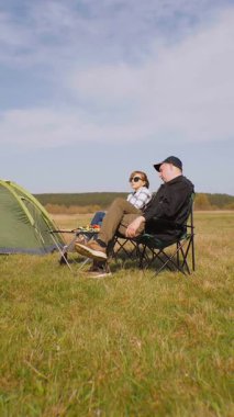 Kafkasyalı rahat bir çift çadırın yanındaki kamp sandalyelerinde oturur ve kupalardan içerler. Güneşli güzel günün ve kırsal alandaki maceralarının tadını çıkarırlar.