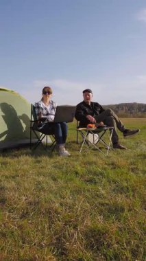 Yeşil bir alanda eşiyle kamp yaparken dizüstü bilgisayarda yazan serbest çalışan bir kadın dijital göçebe yaşam tarzını uzaktan çalışma ve açık hava macera videosuyla kucaklıyor.