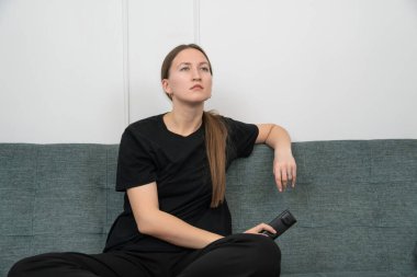 Kanepede bacak bacak bacak üstüne atmış, elinde uzaktan kumandayla oturan ve en sevdiği TV programını eğlence ve rahatlamaya dalmış, rahat bir oturma odasında seyreden rahat bir kadın.