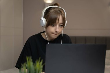 Kulaklık takan genç bir kadın evde çalışıyor, dizüstü bilgisayar kullanıyor ve işine odaklanıyor, esnek çalışma düzeninin ve modern teknolojinin tadını çıkarıyor.