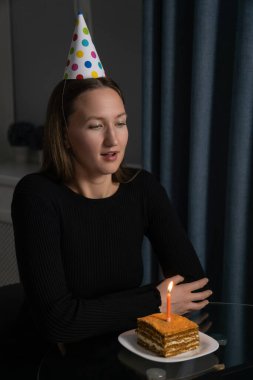 İnternette doğum gününü kutlayan parti şapkası takan genç bir kadın dizüstü bilgisayarla, mumla pasta parçasına bakıyor arkadaşları ve ailesiyle video görüşmesi yapıyor. Dikey fotoğraf